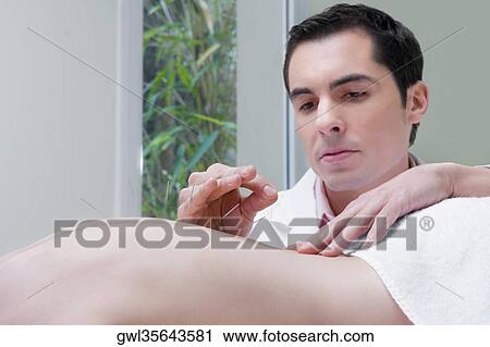 Stock Image - Acupuncturist applying needles on a person's back. Fotosearch