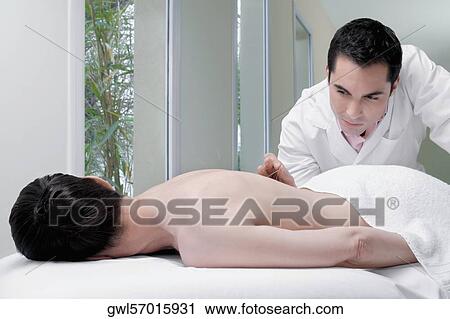 Stock Image - Acupuncturist applying needles on a person's back. Fotosearch