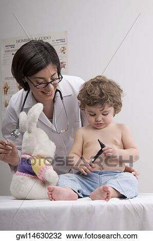 Baby boy holding an otoscope with a female doctor standing behind him View Large Photo Image Stock Image - Baby boy holding an otoscope with a female doctor standing behind him. Fotosearch