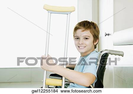 Boy holding crutch and sitting in a wheelchair View Large Photo Image Picture - Boy holding crutch and sitting in a wheelchair. Fotosearch