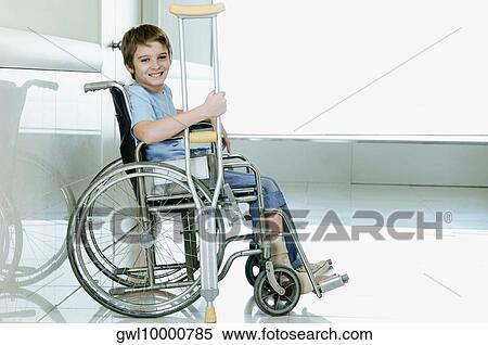 Stock Photography - Boy holding crutch and sitting in a wheelchair. Fotosearch