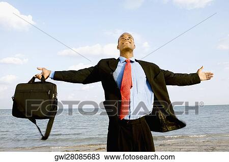 Businessman standing on the beach with his arm outstretched View Large Photo Image Stock Image - Businessman standing on the beach with his arm outstretched. Fotosearch