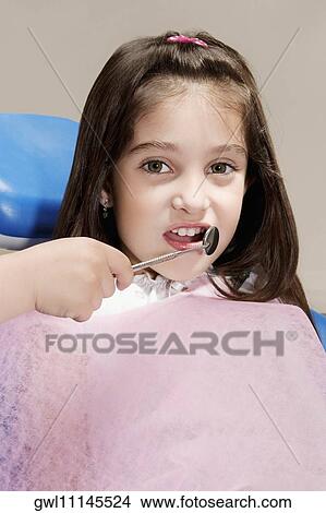 Child's hand holding an angled mirror in front of a girl's teeth View Large Photo Image Picture - Child's hand holding an angled mirror in front of a girl's teeth. Fotosearch