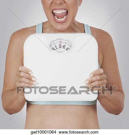 Close-up of a woman holding a bathroom scale and shouting in excitement View Large Photo Image Picture - Close-up of a woman holding a bathroom scale and shouting in excitement. Fotosearch