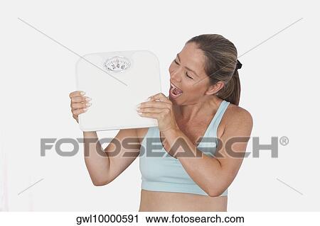Stock Image - Close-up of a woman holding a bathroom scale and looking excited. Fotosearch