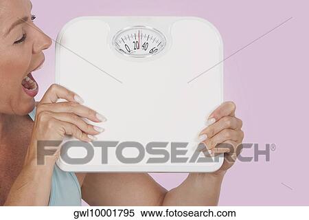 Stock Photography - Close-up of a woman holding a bathroom scale and looking excited. Fotosearch
