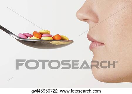 Stock Image - Close-up of a woman with a spoonful of pills. Fotosearch