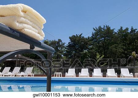 Stock Image - Close-up of towels and lounge chairs at the poolside. Fotosearch