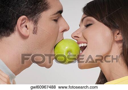 Couple biting into a green apple View Large Photo Image Stock Photo - Couple biting into a green apple. Fotosearch