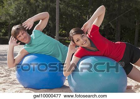Stock Photo - Couple exercising with fitness balls on the beach. Fotosearch