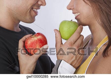 Couple offering apples to each other and smiling View Large Photo Image Stock Photography - Couple offering apples to each other and smiling. Fotosearch