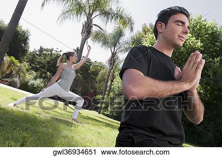 Couple practicing yoga in a park View Large Photo Image Stock Image - Couple practicing yoga in a park. Fotosearch