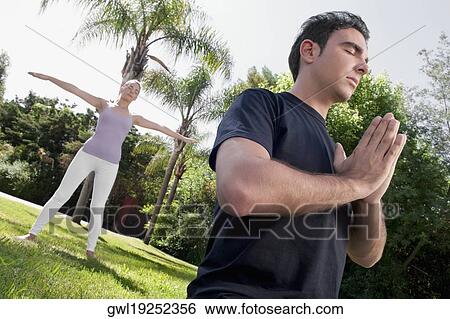 Stock Photograph - Couple practicing yoga in a park. Fotosearch
