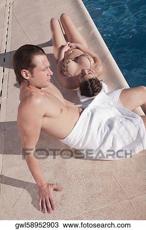 Stock Image - Couple resting by a swimming pool. Fotosearch