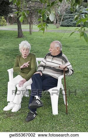 Couple sitting on chairs in a park View Large Photo Image Stock Image - Couple sitting on chairs in a park. Fotosearch