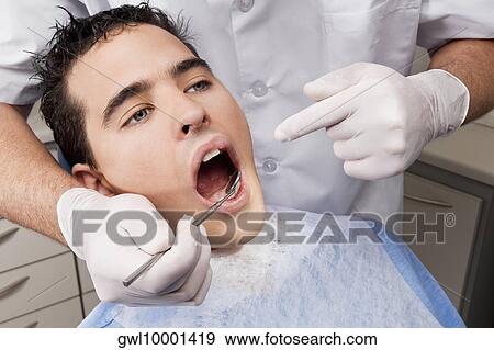 Dentist examining a man's teeth View Large Photo Image Stock Photo - Dentist examining a man's teeth. Fotosearch