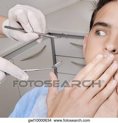 Dentist holding dental equipments while scared patient covering his mouth View Large Photo Image Picture - Dentist holding dental equipments while scared patient covering his mouth. Fotosearch