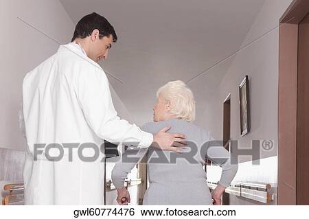 Doctor assisting a woman in walking View Large Photo Image Stock Photograph - Doctor assisting a woman in walking. Fotosearch