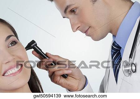 Doctor checking a woman's ear with an otoscope View Large Photo Image Stock Photo - Doctor checking a woman's ear with an otoscope. Fotosearch