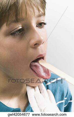Doctor examining a boy's mouth with a tongue depressor View Large Photo Image Stock Photo - Doctor examining a boy's mouth with a tongue depressor. Fotosearch