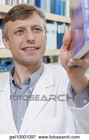 Doctor holding a book and smiling in a laboratory View Large Photo Image Stock Photo - Doctor holding a book and smiling in a laboratory. Fotosearch