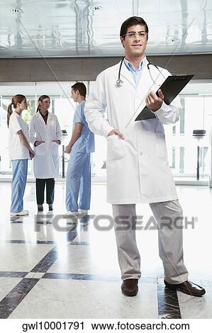 Doctor holding a clipboard with his colleagues discussing in the background View Large Photo Image Stock Image - Doctor holding a clipboard with his colleagues discussing in the background. Fotosearch