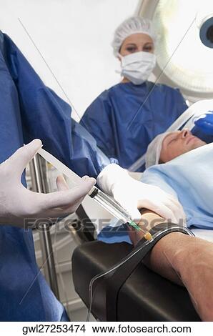 Doctor injecting patient's arm in an operating room View Large Photo Image Picture - Doctor injecting patient's arm in an operating room. Fotosearch