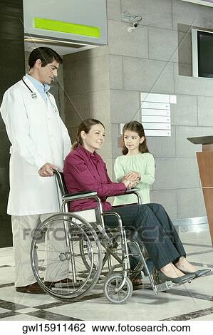 Doctor pushing a woman in a wheelchair View Large Photo Image Stock Image - Doctor pushing a woman in a wheelchair. Fotosearch