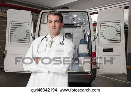 Picture - Doctor standing with an ambulance behind him. Fotosearch