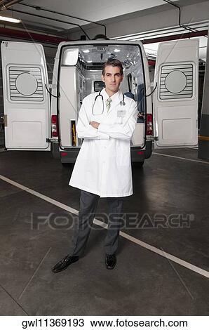 Stock Image - Doctor standing with an ambulance behind him. Fotosearch