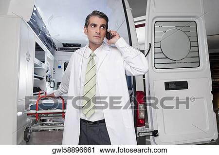 Doctor talking on a mobile phone in front of an ambulance View Large Photo Image Stock Image - Doctor talking on a mobile phone in front of an ambulance. Fotosearch