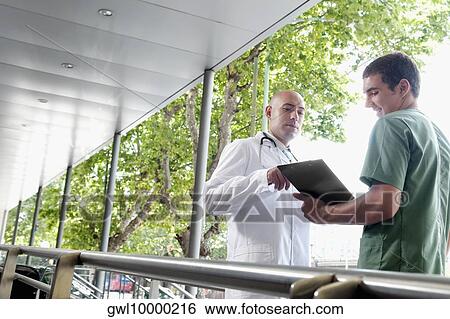 Doctor talking to a male nurse View Large Photo Image Stock Photograph - Doctor talking to a male nurse. Fotosearch