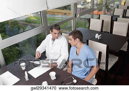 Doctors discussing a medical report in a cafeteria View Large Photo Image Stock Image - Doctors discussing a medical report in a cafeteria. Fotosearch