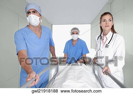 Doctors pushing a patient on a hospital Gurney in a hospital corridor View Large Photo Image Stock Photo - Doctors pushing a patient on a hospital Gurney in a hospital corridor. Fotosearch