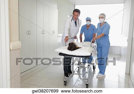 Doctors pushing a patient on a hospital Gurney in a hospital corridor View Large Photo Image Stock Photo - Doctors pushing a patient on a hospital Gurney in a hospital corridor. Fotosearch