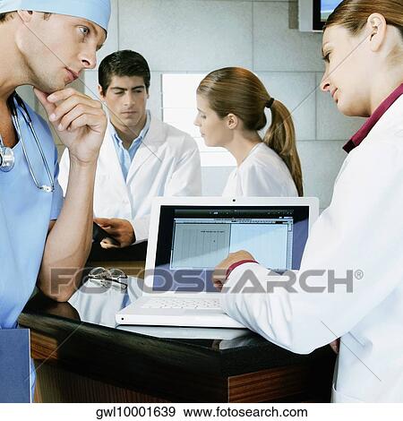 Stock Photo - Female doctor and a surgeon discussing a medical report on a laptop. Fotosearch