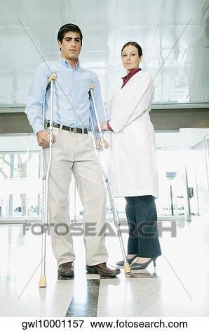 Female doctor assisting a man on crutches View Large Photo Image Stock Photo - Female doctor assisting a man on crutches. Fotosearch