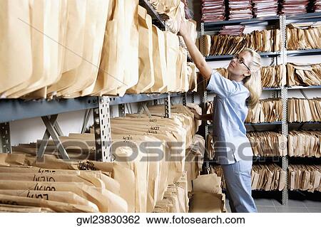Female doctor checking records in a record room View Large Photo Image Stock Image - Female doctor checking records in a record room. Fotosearch