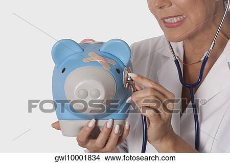 Female doctor examining a piggy bank with a stethoscope View Large Photo Image Picture - Female doctor examining a piggy bank with a stethoscope. Fotosearch