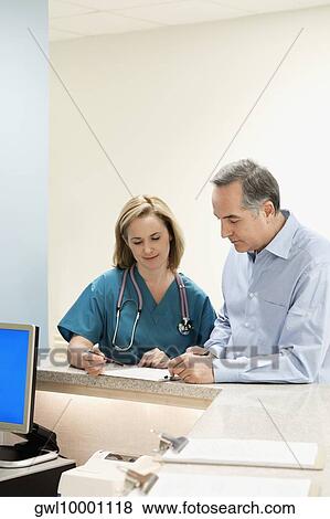 Female doctor examining a report with a patient standing beside her at a reception counter in a hospital View Large Photo Image Stock Photo - Female doctor examining a report with a patient standing beside her at a reception counter in a hospital. Fotosearch