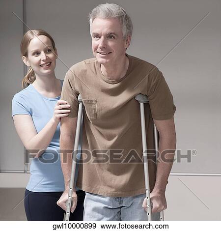 Stock Photo - Female doctor helping man walk with crutches. Fotosearch