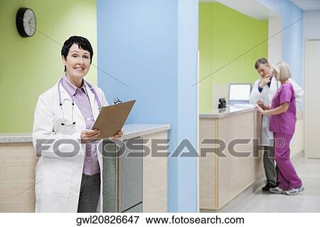Female doctor holding a clipboard with a doctor and nurse in the background View Large Photo Image Stock Photo - Female doctor holding a clipboard with a doctor and nurse in the background. Fotosearch