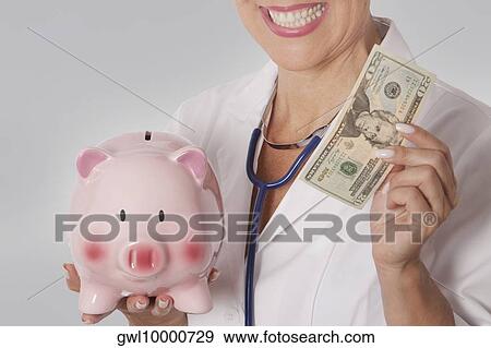Female doctor holding a currency note and a piggy bank View Large Photo Image Stock Photo - Female doctor holding a currency note and a piggy bank. Fotosearch