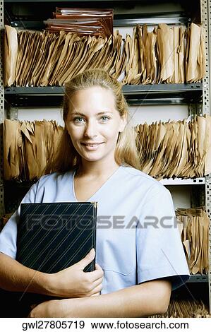 Female doctor holding a file in a record room View Large Photo Image Stock Photo - Female doctor holding a file in a record room. Fotosearch
