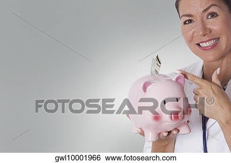 Female doctor holding a piggy bank with currency note View Large Photo Image Stock Photograph - Female doctor holding a piggy bank with currency note. Fotosearch
