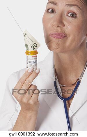 Female doctor holding a pill bottle with currency note View Large Photo Image Stock Image - Female doctor holding a pill bottle with currency note. Fotosearch