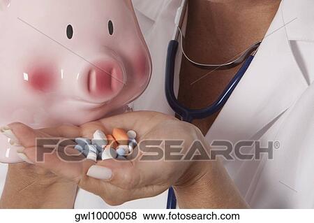 Female doctor holding pills in front of a piggy bank View Large Photo Image Stock Photo - Female doctor holding pills in front of a piggy bank. Fotosearch