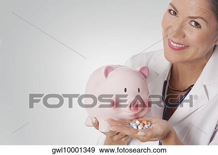 Female doctor holding pills in front of a piggy bank View Large Photo Image Stock Photo - Female doctor holding pills in front of a piggy bank. Fotosearch