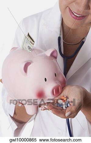 Female doctor holding pills in front of a piggy bank View Large Photo Image Stock Photography - Female doctor holding pills in front of a piggy bank. Fotosearch