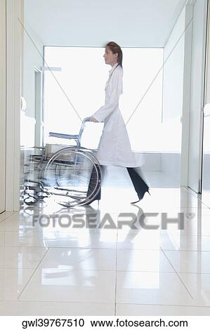 Stock Image - Female doctor pushing an empty wheelchair. Fotosearch